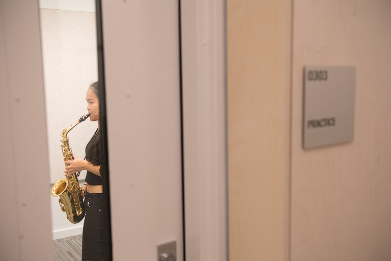A student playing saxophone in a private practice room