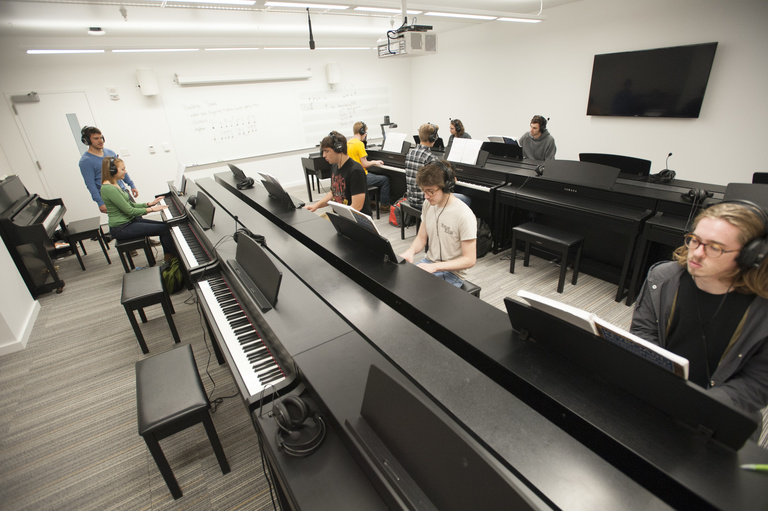 Students practicing in a piano lab led by an instructor