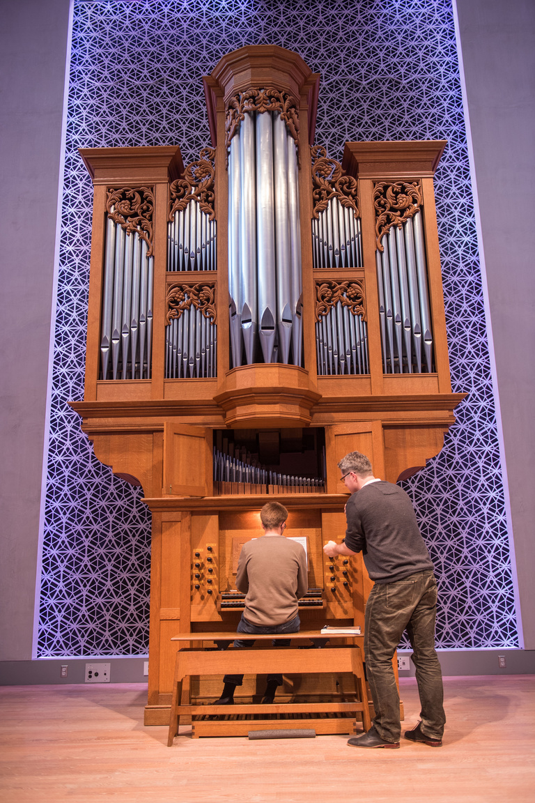 A wide view of a large pipe organ being played by a student with an instructor behind them