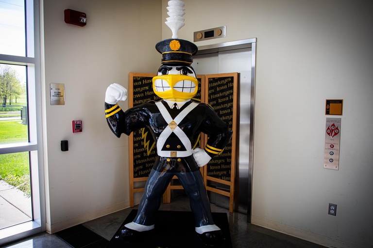 Alumni Band Herky fully costumed in the original Marching Band Uniform from the 1940s and 50s. The outfit includes a hat with a tall white feather, a black military looking coat with two gold bands around the wrist, and white straps that cross in the front as well as buckles on Herkys shoulder. He also wears white gloves. 