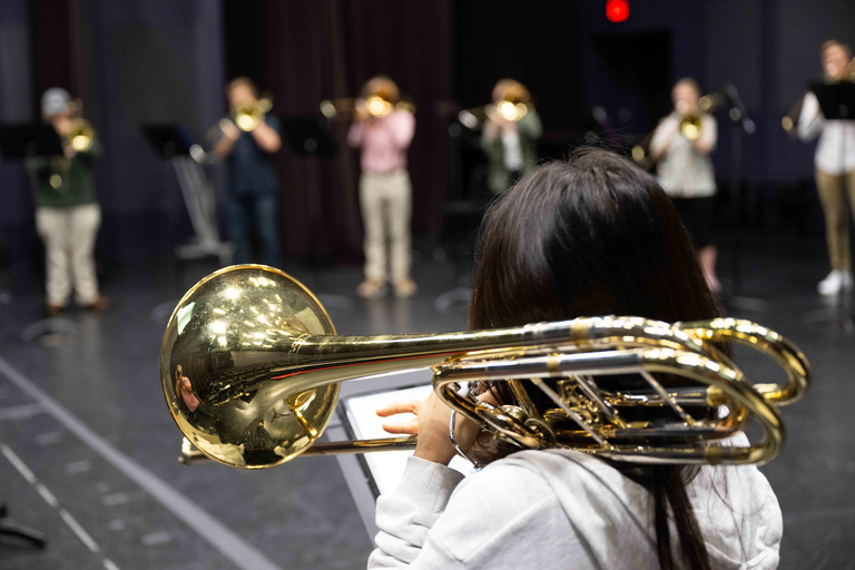 A student viewed from behind, playing the trombone in a class in Stark Opera Studio