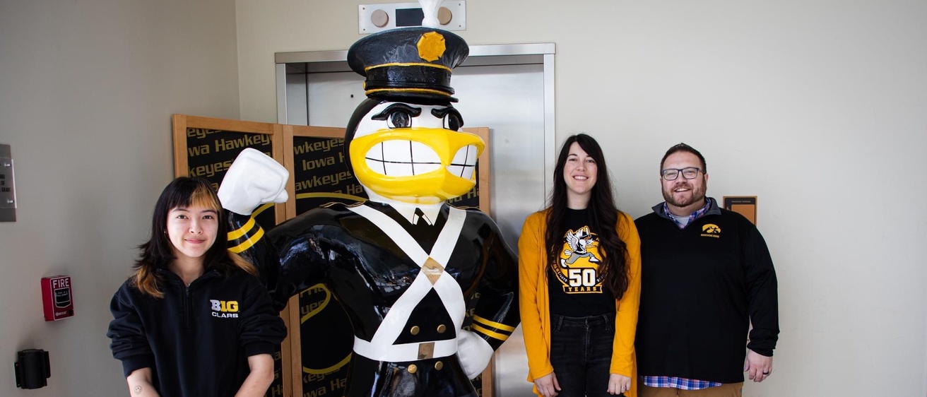 Artists Mae Dunning in black pull-over and jeans, Amanda Stout to Herky's right in yellow cardigan over the Alumni Band's 50th Anniversary t-shirt, and Marching Band Director Dr. Eric Bush in black pull over and khaki pants posing with the completed Alumni Band Herky for Herky on Parade. The Alumni Marching Herky is center, fully costumed in the original Marching Band Uniform from the 1940s and 50s. 