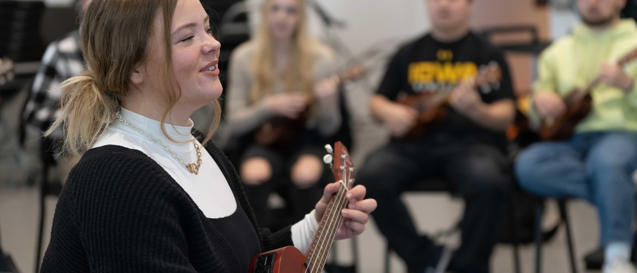 Music Education students in a Voxman classroom. The woman student in the foreground is playing a ukulele and singing.