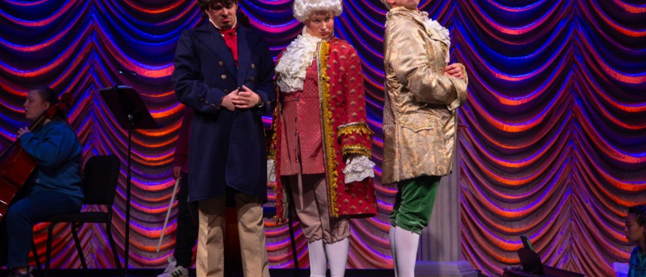 The Classical Style dress rehearsal with performers portraying Mozart, Beethoven, and Haydn stand together on stage making comedic judgemental expressions.