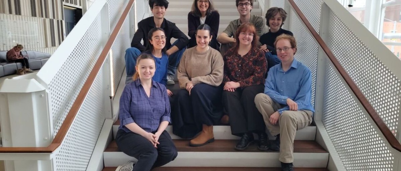 Beth Oakes and eight of her students sitting on the stairs in Voxman Music Building