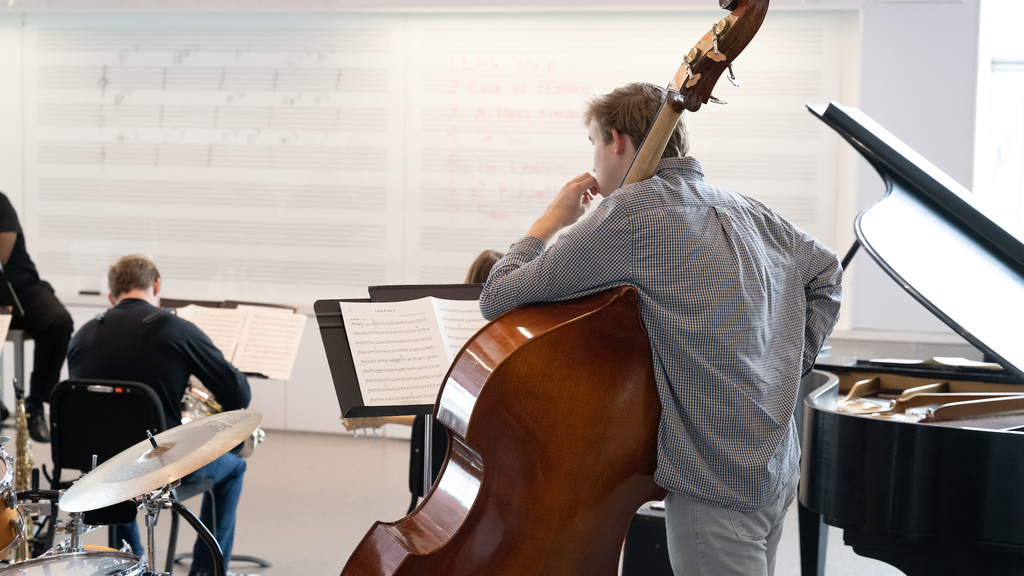 student musician leaning on his double bass in a Voxman Music Building classroom