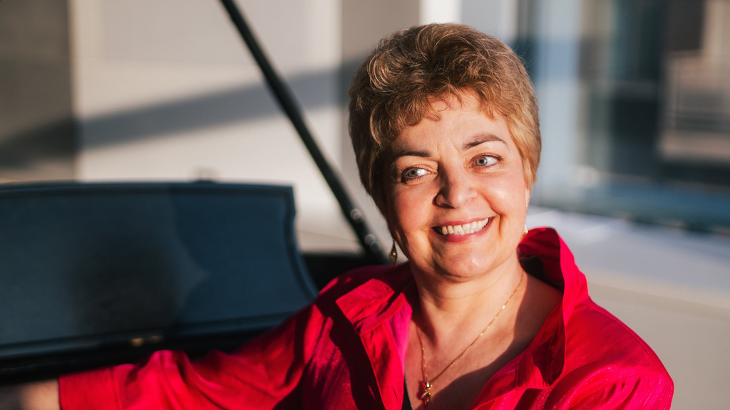 Ksenis Nosikova in a red blouse, seated at a grand piano