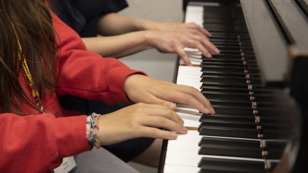 two pairs of hands on a piano keyboard