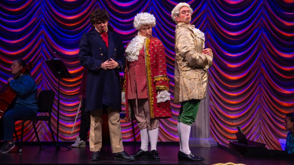 The Classical Style dress rehearsal with performers portraying Mozart, Beethoven, and Haydn stand together on stage making comedic judgemental expressions.