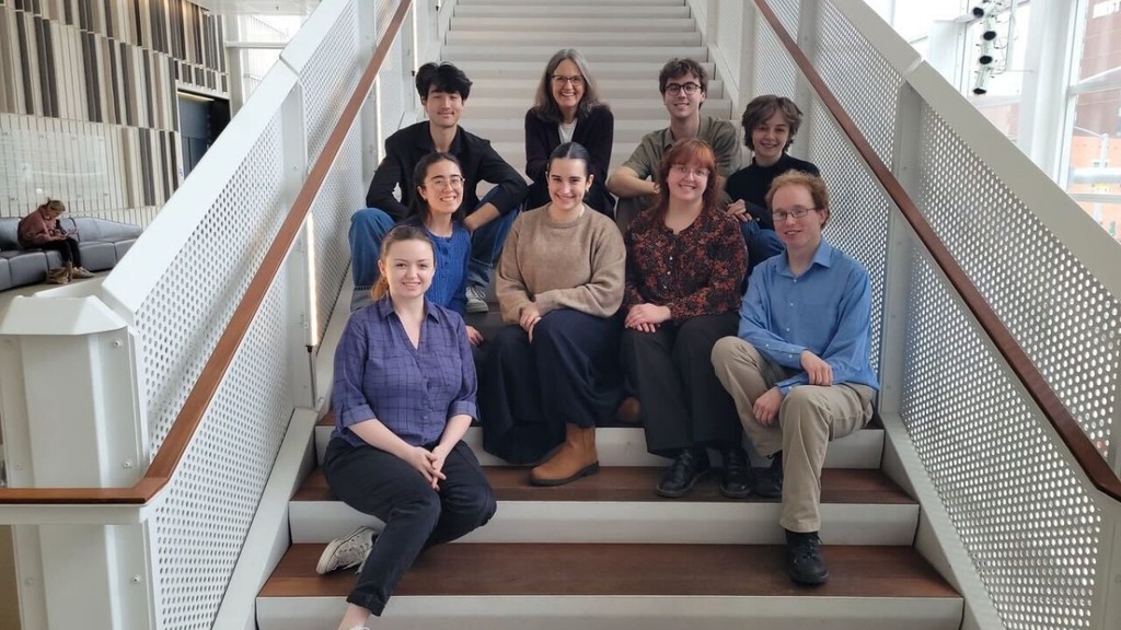 Beth Oakes and eight of her students sitting on the stairs in Voxman Music Building