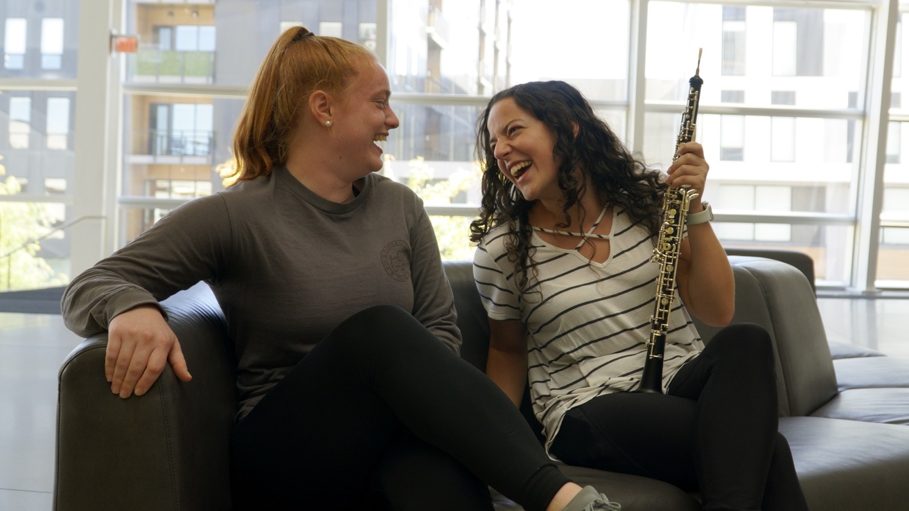 two oboe students laughing while sitting on a couch in the Pearl Lobby of Voxman